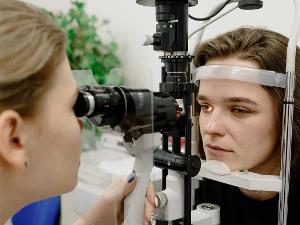 Ärztin untersucht eine Patientin und schaut ihr mit einem Gerät ins Auge.