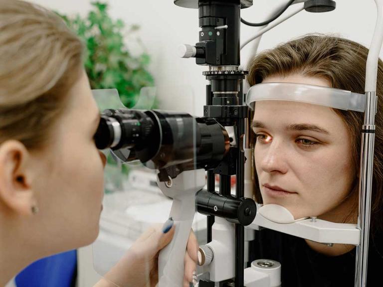 Ärztin untersucht eine Patientin und schaut ihr mit einem Gerät ins Auge.