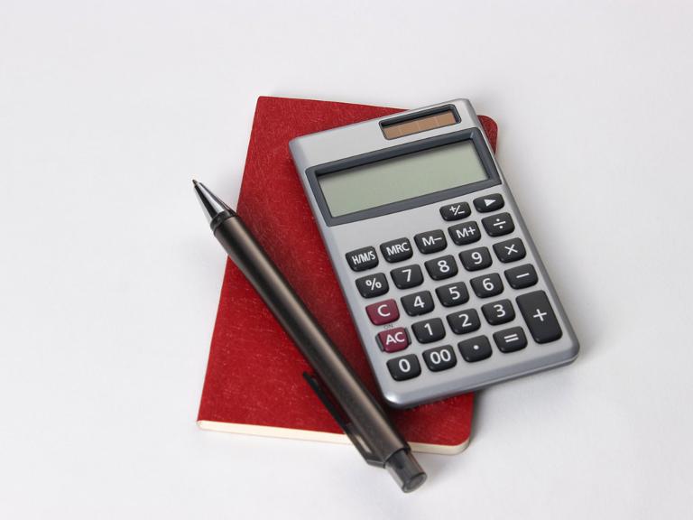 Ein Taschenrechner und ein Stift liegen auf einem kleinen, roten Notizbuch