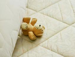 Brauner Teddy liegt auf einer weißen Matratze.