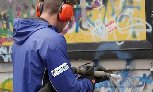 Mann mit Gehörschutz entfernt Graffiti von einer Wand mit trockeneisstrahlen