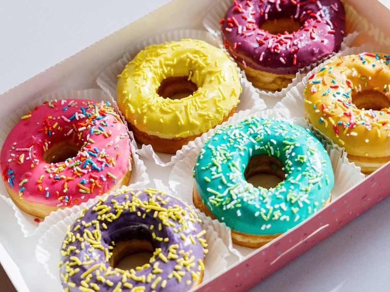 Sechs bunt dekorierte Donuts in einer rosafarbenen Schachtel