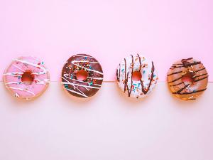 Vier Donuts mit Schokolade und Streuseln liegen nebeneinander auf rosafarbenem Untergrund