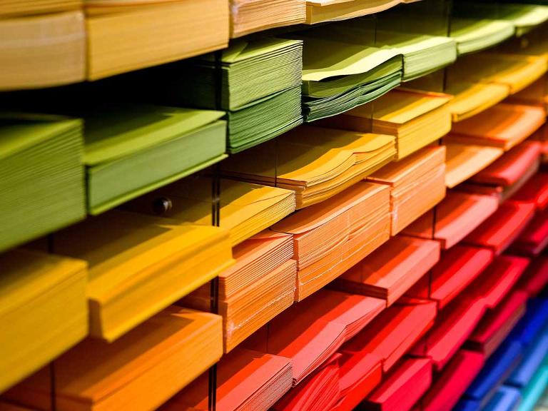 Papier in verschiedenen Farben liegt sortiert in dafür vorgesehene Fächer in einem Regal