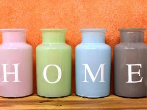 Vier unteschiedlich farbige Vasen stehen nebeneinander, jede hat einen Buchstaben aufgedruckt, diese ergeben das Wort HOME