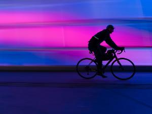 Ein Mensch fährt auf einem Rennrad an einer bunt beleuchteten Wand entlang