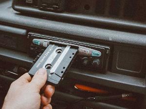 Ein Mensch schiebt eine Kassette in die dafür vorgesehene Öffnung in einem Autoradio