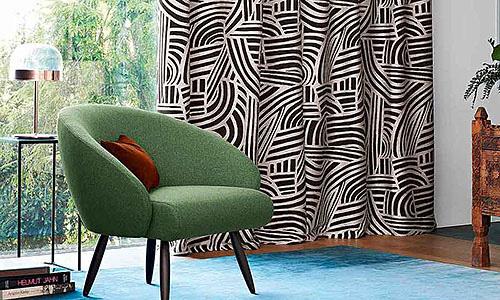 Gemusterte Vorhänge und ein grüner Sessel auf einem türkisfarbenen Teppich