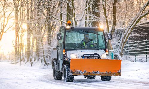 Einsatzfahrzeug fährt durch ein verschneites Waldstück bei Tag.
