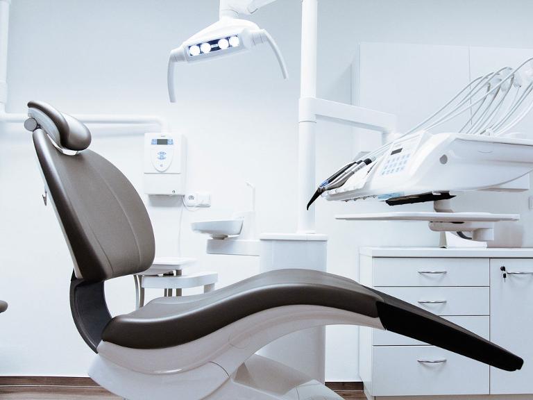 Zahnarztstuhl im Behnandlungsraum mi technischen Geräten im Hintergrund