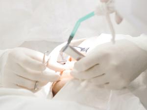 Arzt mit weißen Handschuhen und weißem Kittel behandelt einen Patienten im Mundbereich.