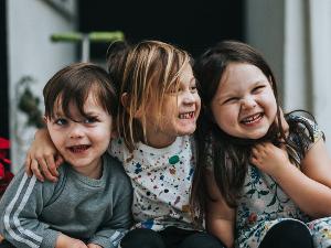 Drei kleine Kinder lachen in die Kamera und zeigen ihre Zähne