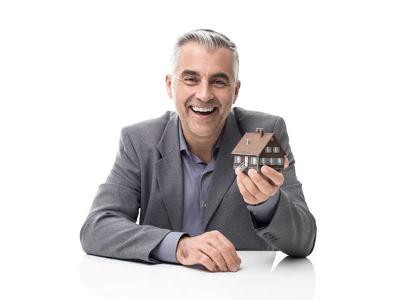 Ein Mann hält eine kleine Nachbildung eines Hauses in der Hand und lächelt in die Kamera