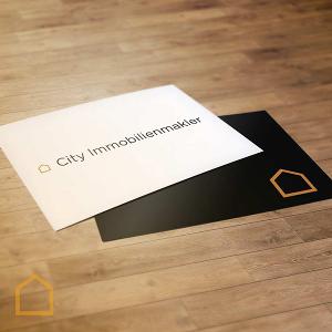 Eine weiße und eine schwarze Postkarte mit dem City Immobilienmakler Logo darauf