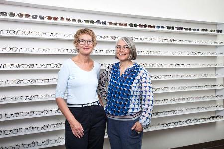 Zwei Frauen stehen vor einer Wand mit Brillen