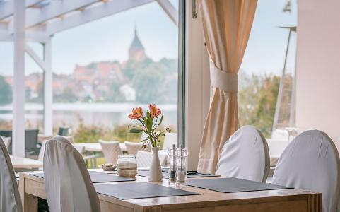 Stühle mit weißen Hussen stehen an einem Tisch, im Hintergrund, auf der anderen Wasserseite ist die Stadt Mölln zu sehen