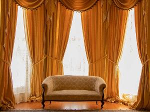 Orangene Gardinenschals zusammengebunden an einer großen Fensterfront, davor steht ein Sofa