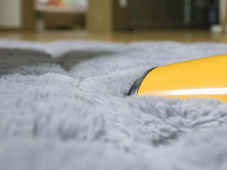 Eine gelbe Staubsaugerbürste auf einem flauschigen hellgrauen Teppich