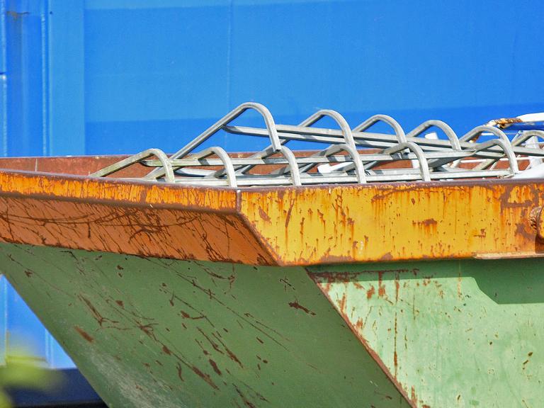 Grüner Container mit Bauschutt vor blauer Wand.