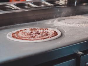 Pizzateig mit Tomatensauce belegt und wird gerade bestreut mit Parmesan, auf einer Arbeitsfläche liegend