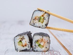 Zwei Sushi auf weißem Untergrund und ein Sushistück wird gehalten von Stäbchen