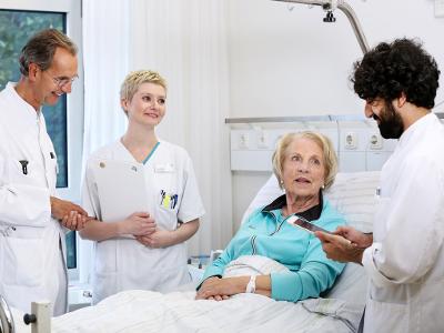Drei Ärzte stehen am Krankenbett einer älteren Dame und unterhalten sich