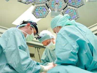 Drei Ärzte in grünen Kitteln operieren unter einer Lampe