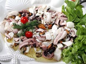 Tintenfischsalat garniert mit Dill, Tomaten und Salat auf einem weißen Teller