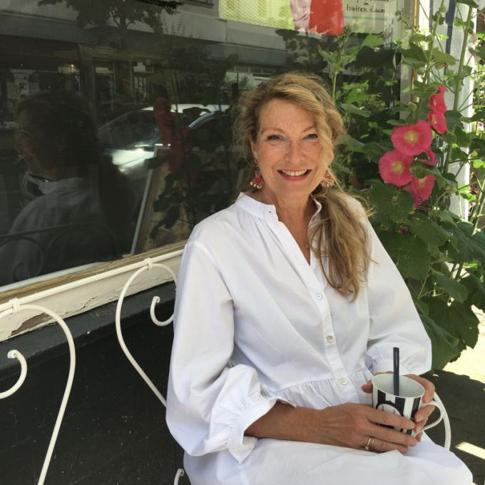 Birgit Kussmaul-Basedahl sitzt auf einer Bank vor ihrem Laden B.Sweet in weißem Kleid