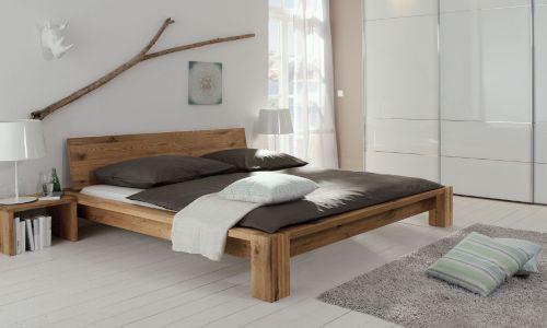 Zimmer mit einem Massivholzbett, mit einem Nachttisch und einem Ast der über dem Bett hängt