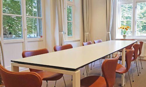 Seminarraum mit langem Tisch und orangenen Stühlen