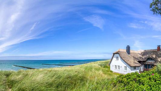 Ein Reetdachhaus in den Dünen unter blauem Himmel am Wasser