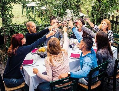 Menschen sitzen an einem Tisch, im Garten und stoßen mit Wein an