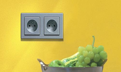 Doppelsteckdose an einer gelben Wand, davor steht eine Schale mit grünen Weintrauben