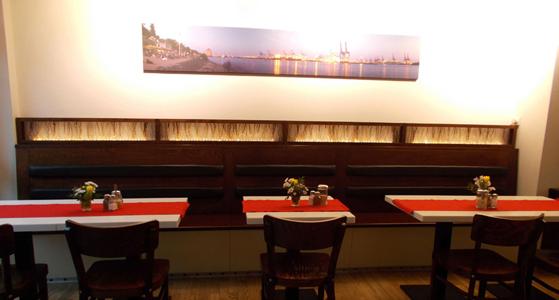 Innenräume des Schanzenstern, Tische und Stühle vor einer Wand mit einem Bild an der Elbe darüber hängend