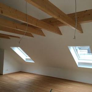 Ein Dachboden mit zwei Fenstern und Dachbalken aus Holz