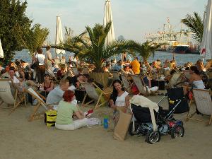 Leute sitzen auf Liegen am Strand mit Blick auf dem Hamburger Hafen