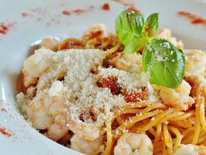 Spaghetti mit Tomatensauce und Shrimps auf einem weißen, tiefen Teller, mit Parmesan und Basilikum als Topping