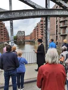 Kaufmann Jacob Lange erklärt Gästen von einer Brücke aus Fleete und Speicherstadt