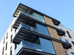 Wohnhaus mit Balkonen und Teilen aus Glas und Holz, unter einem blauen Himmel