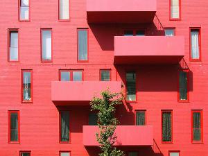 Eine komplett rote Häuserfassade mit roten Balkonen, roten Rahmen um die Fenster und einem grünen Baum in der Mitte