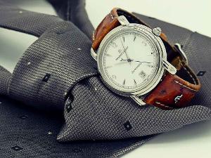 Eine Armbanduhr aus braunem Leder mit silbernem Ring um das weiße Ziffernblatt liegt auf einer grauen Krawatte