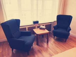 Zwei Sessel stehen links und rechts von einem kleinen Holztisch, vor einem Fenster und auf einem Holzfußboden