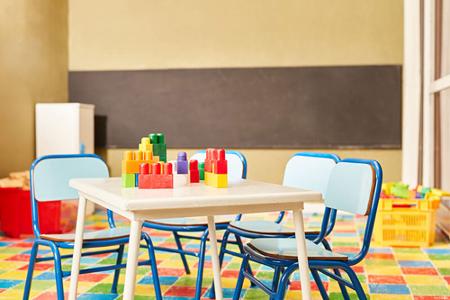 Ein kleiner Tisch mit Spielsachen drauf und drumherum vier blaue Stühle in einem Kindergarten