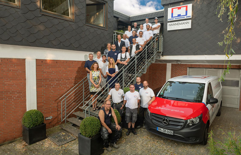 Außenbereich der Firma Stefan Hannemann GmbH, die Mitarbeiter stehen auf einer Treppe und unten neben dem Firmenauto