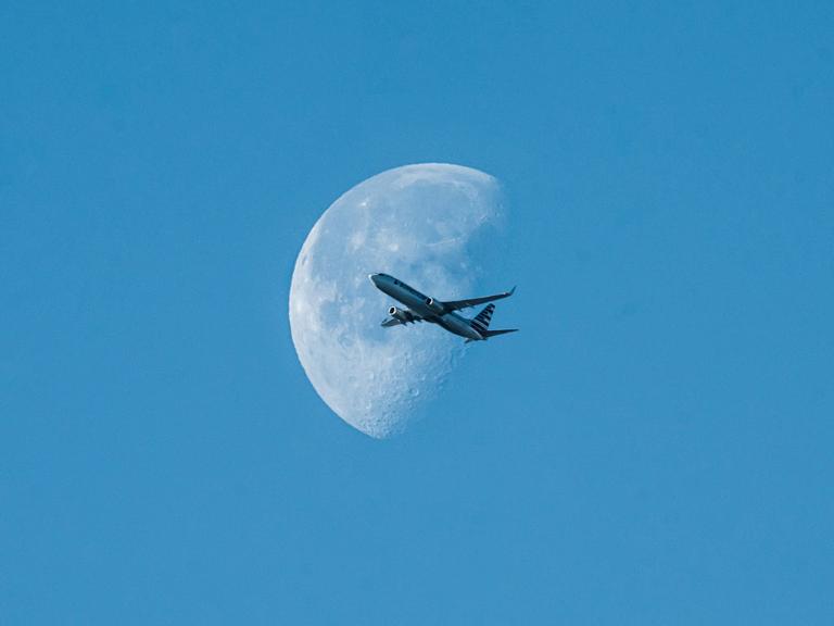 Ein Flugzeug am blauen Himmel vor einem blassen Mond
