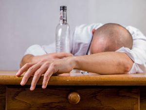 Ein Mann hält liegt mit dem Kopf auf dem Tisch und hält mit der einen Hand eine leere Glasflasche fest