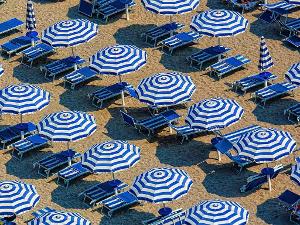 Luftaufnahme von blauweißen Sonnenschirmen neben Liegen an einem Strand
