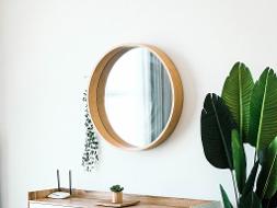 Ein runder Spiegel mit Holzrahmen hängt an einer weißen Wand über einem Holzsideboard und neben einer grünen Pflanze