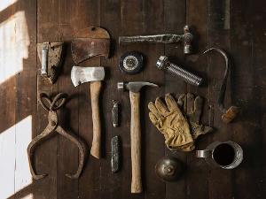 Verschiedene Werkzeuge und Arbeitshandschuhe liegen auf einer dunklen Holzplatte